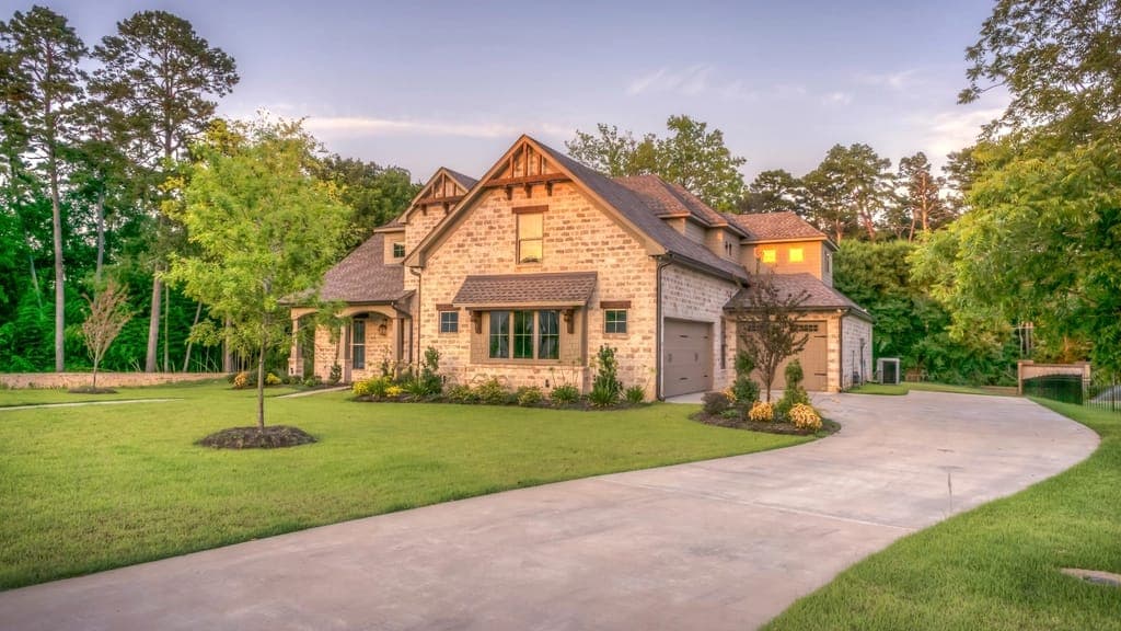 Stone house at dusk with a long curving concrete driveway and a green lawn