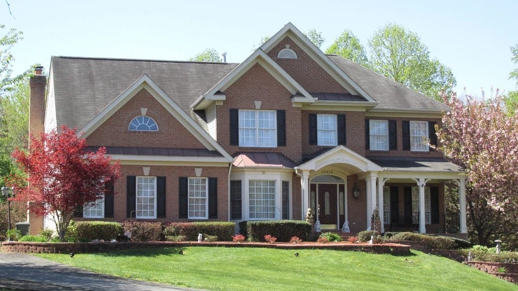Large red brick house with black shutters above a sloped lawn and flowering trees