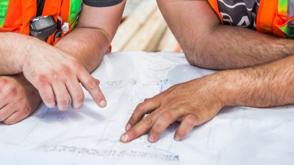 Two people in high-visibility vests pointing at a printed plan on a table